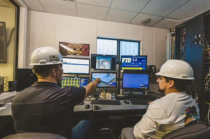 Two people in hard hats in the Wall of Wind control room