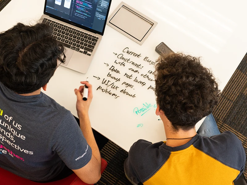an overview of two students using a laptop and writing on a whiteboard