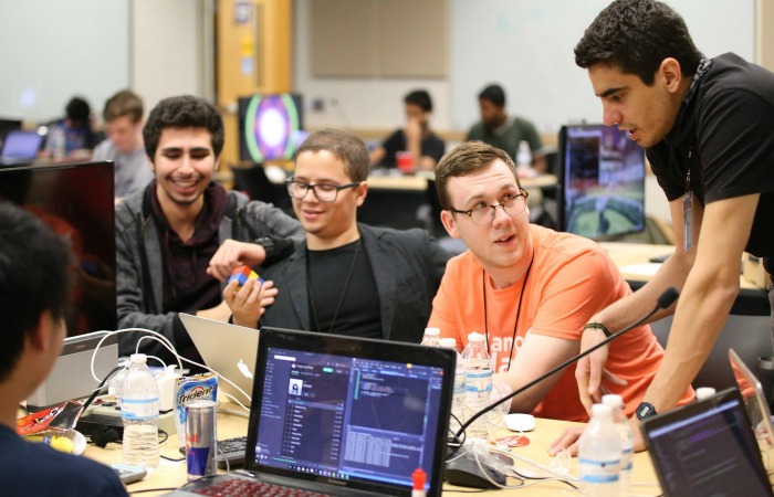 MangoHacks mentor Jacob Jenkins (center, orange shirt) brainstorms with attendees Baruch Hen (left) and FIU students Jose Morgan (center, dark jacket) and Lukas Borges (right, standing).